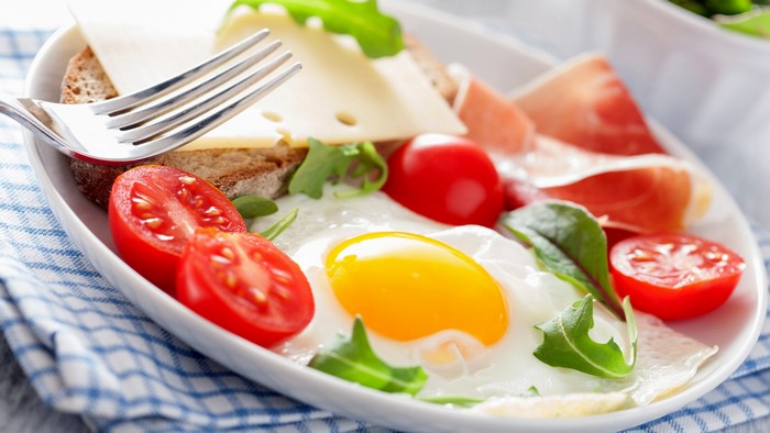 Breakfast plate with fried egg, tomatoes, cheese, bread, and prosciutto