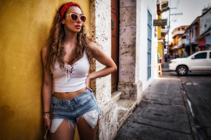 Woman in shorts and white top posing by yellow wall