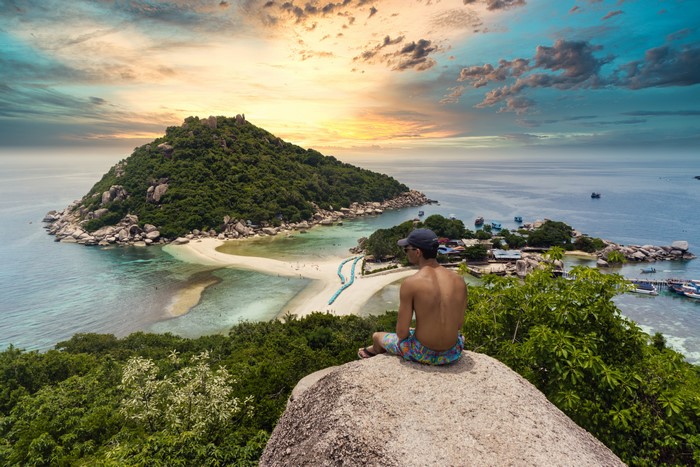 Man sitting on a rock overlooking an island in Thailand