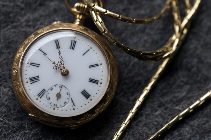 Gold pocket watch with chain on dark background