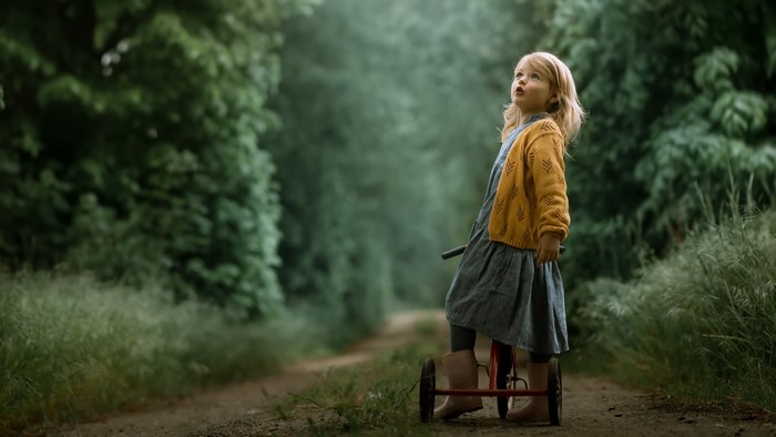 Little girl on a tricycle in a forest path