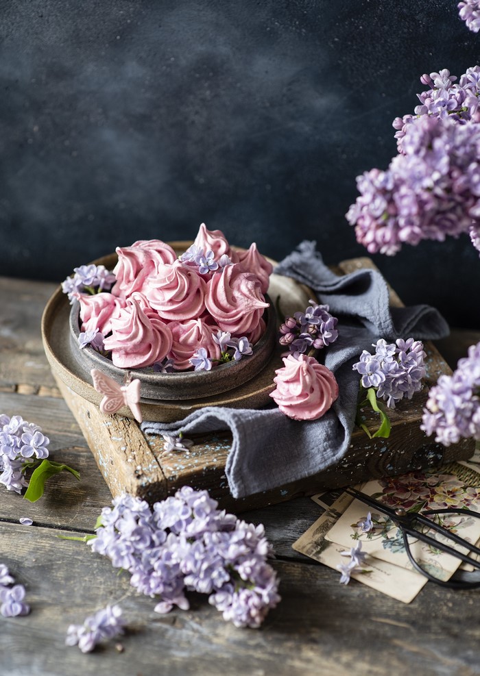 Pink meringues with lilac flowers on a wooden board