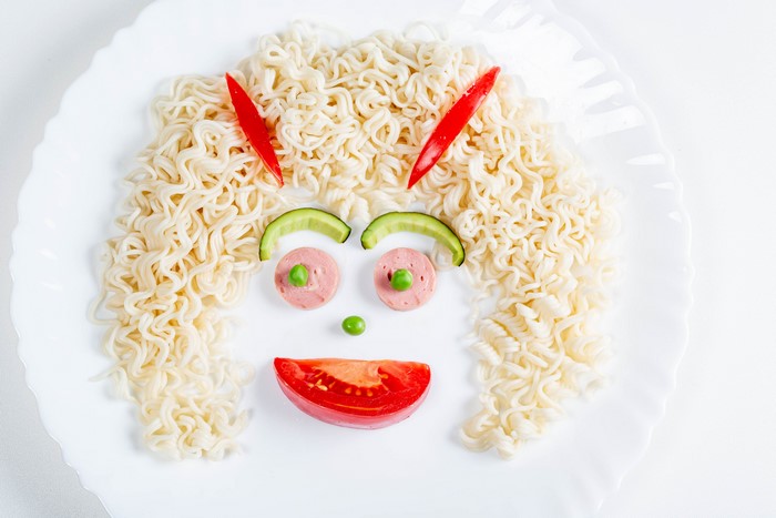 Creative face made of noodles and vegetables on a plate