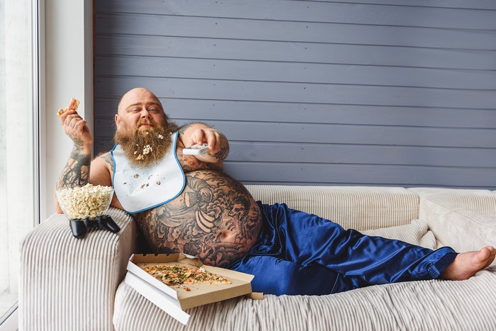Fat Man with Beard Eating Pizza and Popcorn on Sofa