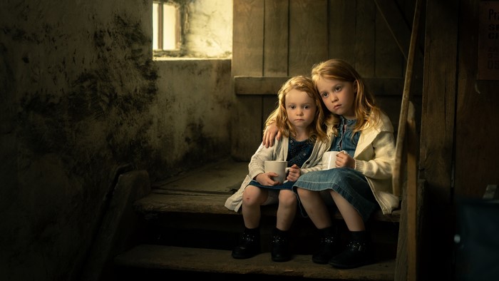 Two sad little sisters sitting on stairs with mugs