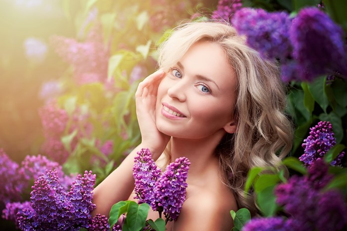 Blonde woman with blue eyes among lilacs