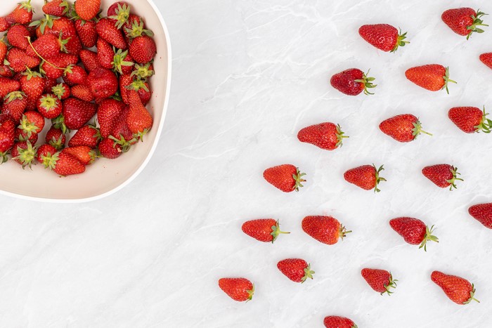 Strawberries in a bowl and scattered on a white background