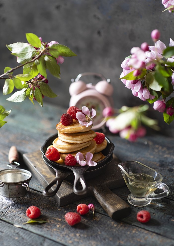 Pancakes with raspberries and flowers on a wooden table