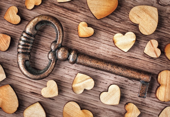 Antique key surrounded by wooden hearts on a wooden surface