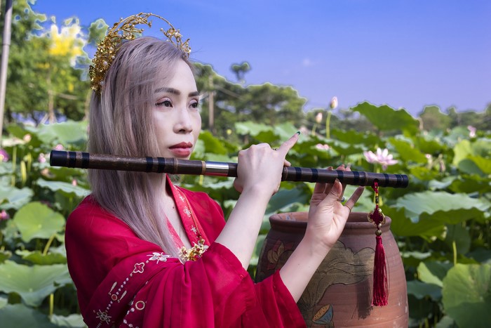 Woman playing flute in lotus pond