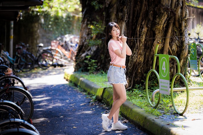 Asian girl in pink t-shirt and denim shorts posing near bicycles