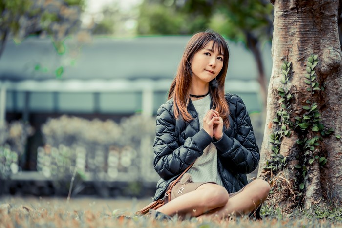 Asian woman sitting by a tree trunk