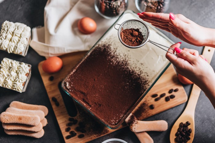 Hands sifting cocoa powder onto tiramisu