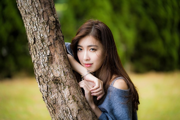 Asian woman with brown hair leaning on a tree trunk