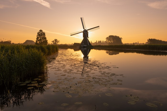 Windmill reflecting in canal at sunrise in Overslingeland, Netherlands