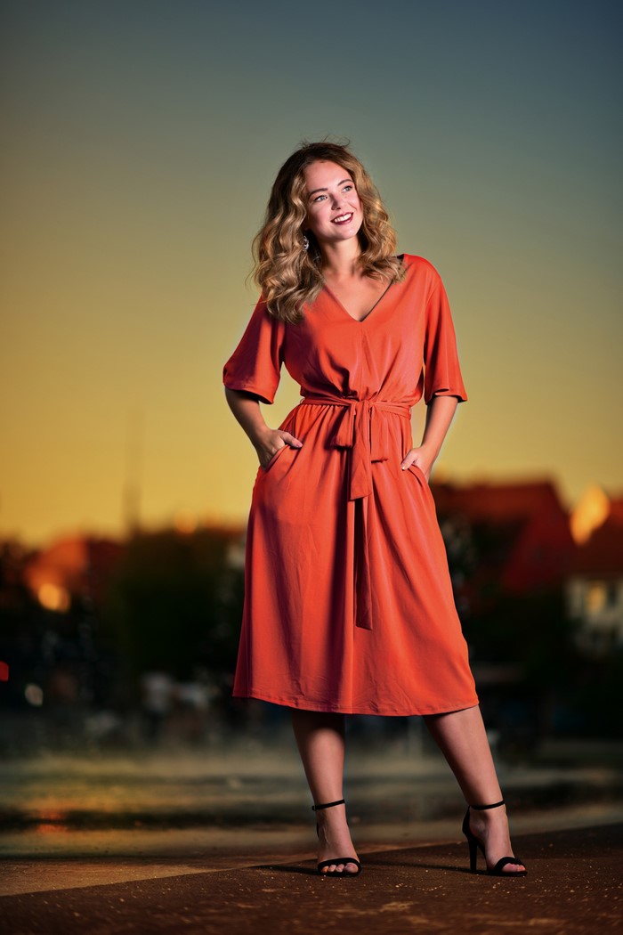 Selina in an orange dress posing at sunset