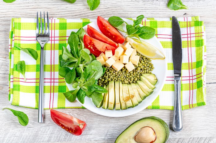 Salad with tomatoes, cheese, avocado, and mung beans on a plate with fork and knife