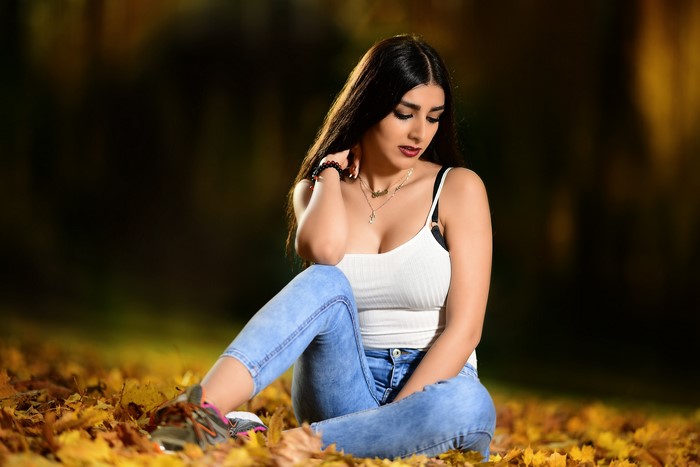 Woman in white singlet and jeans sitting on autumn leaves