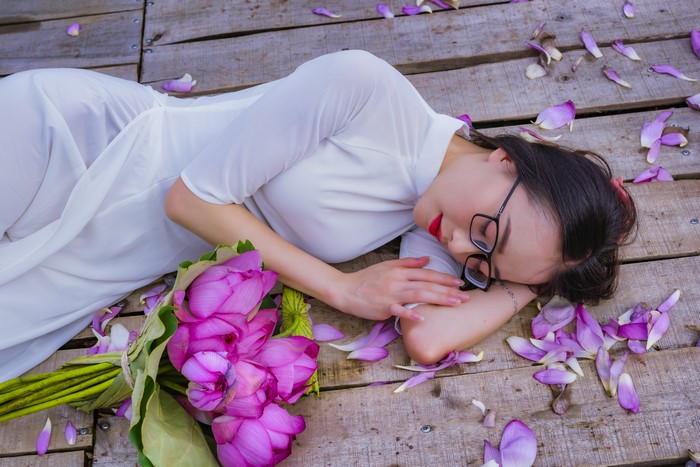 Brunette girl in white dress with lotus bouquet on wood planks