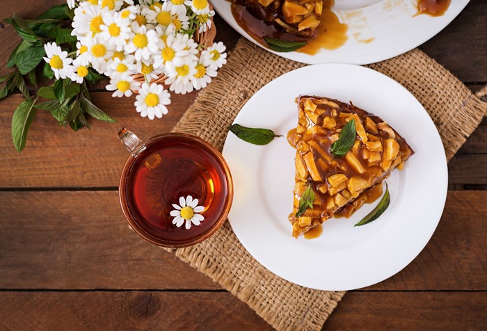 Slice of pie with caramel and nuts, chamomile tea and flowers