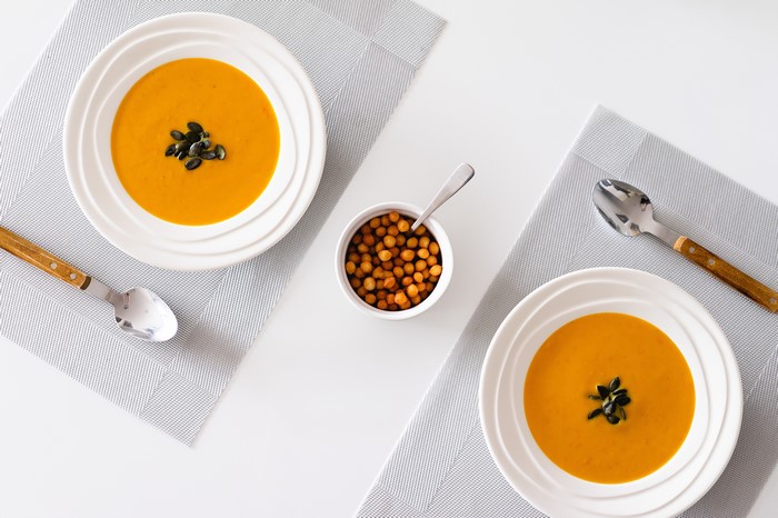 Two bowls of pumpkin soup with pumpkin seeds and croutons