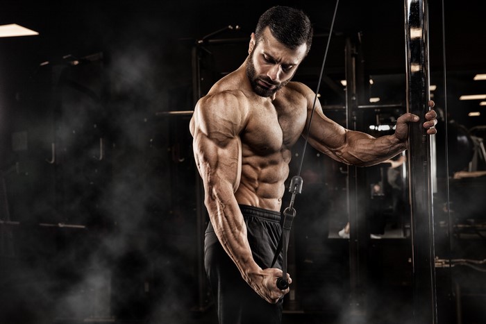 Muscular man performing cable triceps pushdown in gym