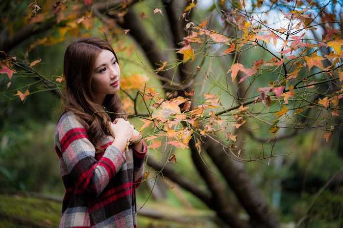 Asian woman in plaid coat among autumn branches