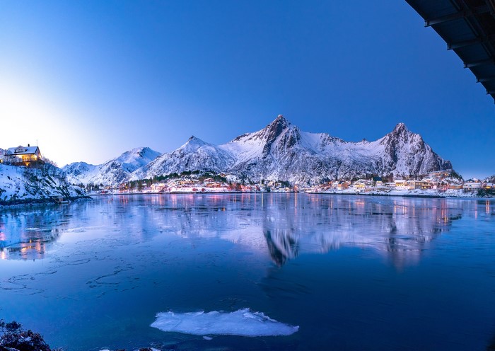 Winter village and snow-capped mountains reflected in a bay