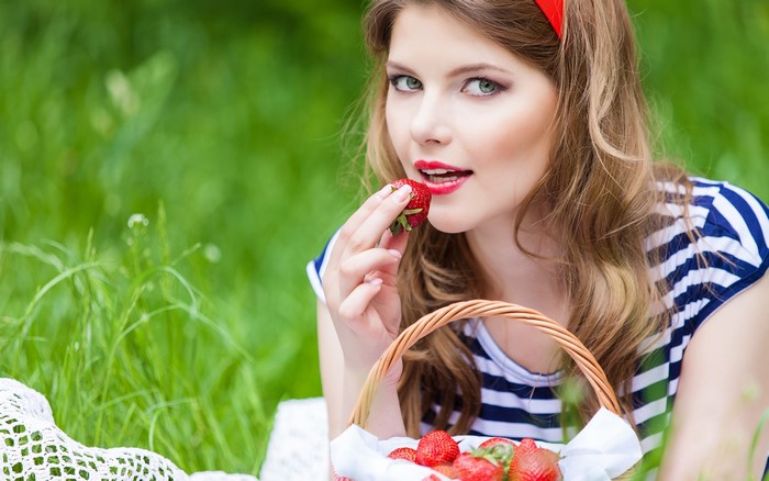 Woman eating strawberry from basket in a field