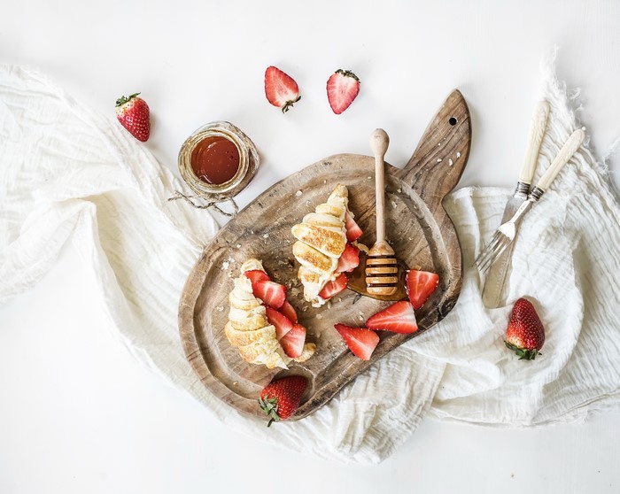 Croissants with strawberries and jam on a cutting board
