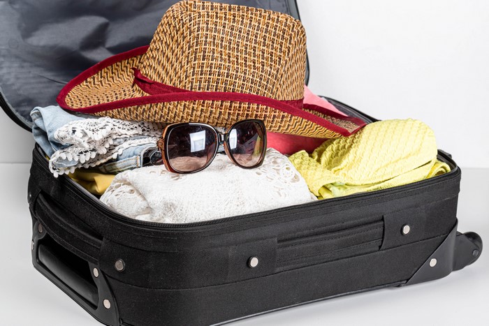 Suitcase packed with clothes, hat, and sunglasses