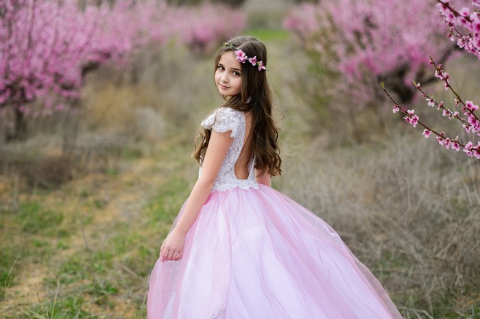 Girl in a pink dress with a flower crown in a blooming orchard