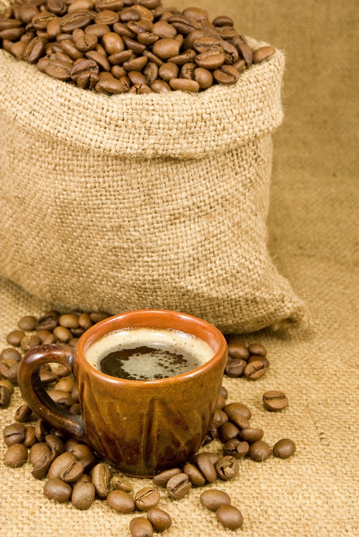 Coffee beans in a burlap sack with a mug of coffee