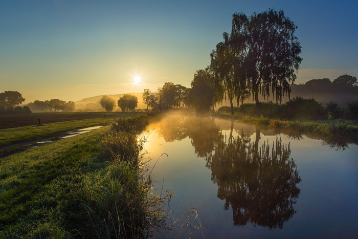 Misty morning sunrise over a canal with trees and reflections