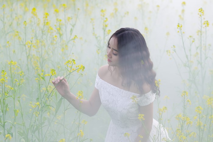 Asian woman in white dress in foggy field of yellow flowers