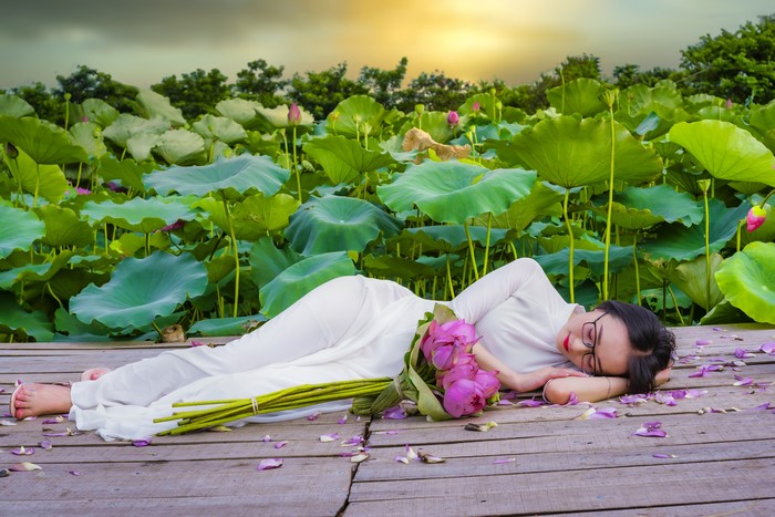 Brunette girl in white dress with lotus bouquet