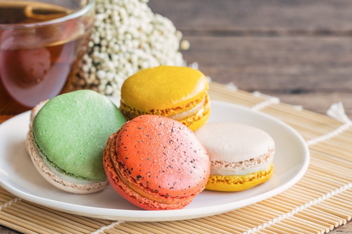 Four colorful macarons on a plate with tea
