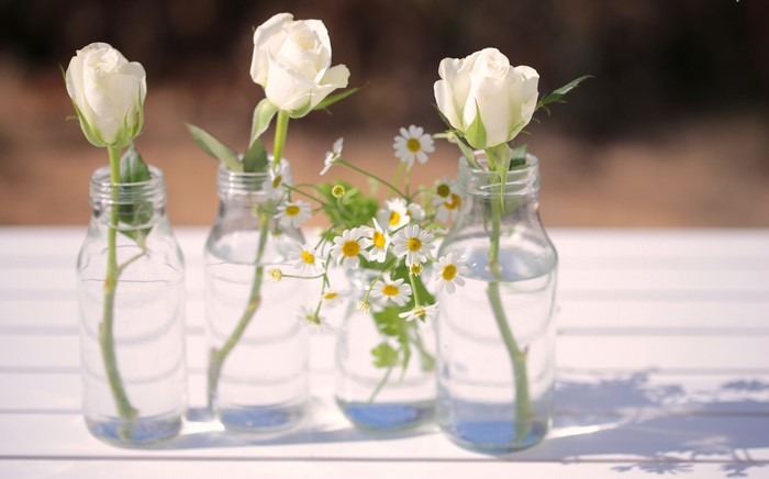 White roses and daisies in glass bottles