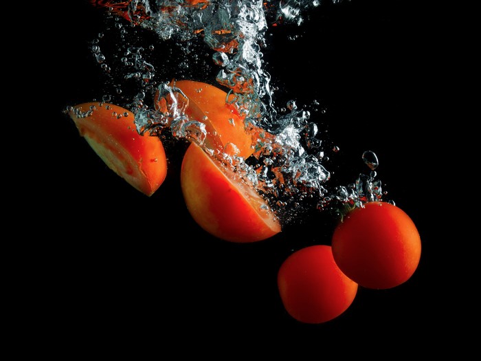 Tomatoes splashing into water on black background