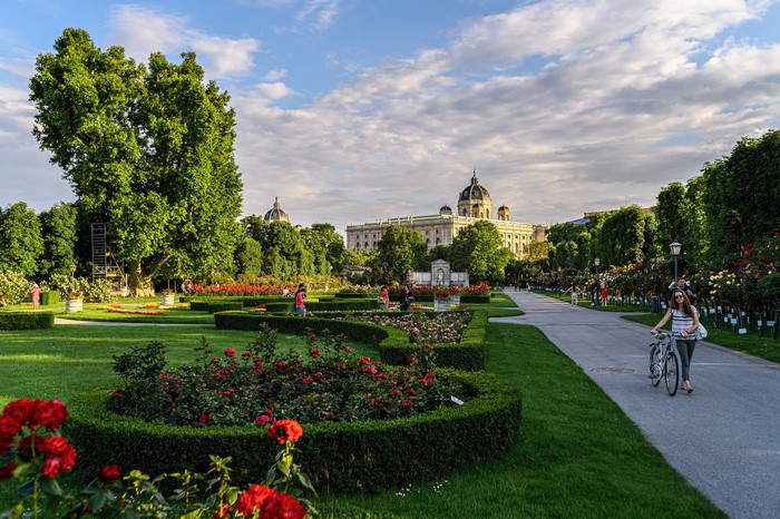 People walking and cycling in a formal garden with a building in the background
