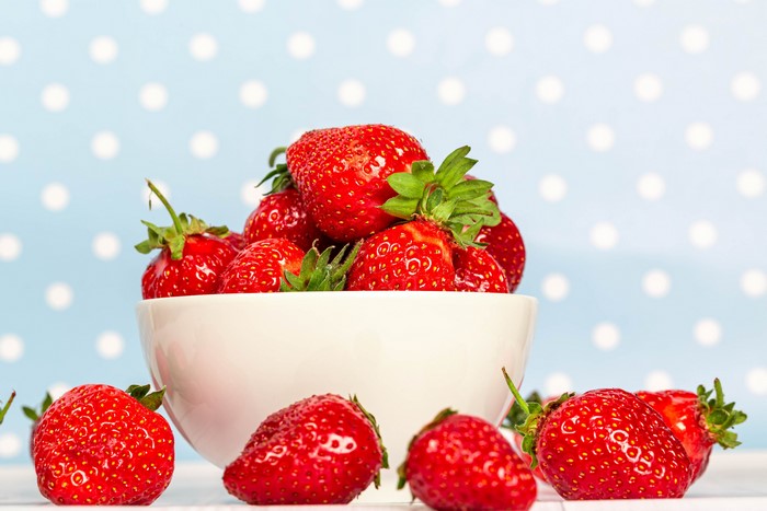 Strawberries in a white bowl on a blue polka dot background