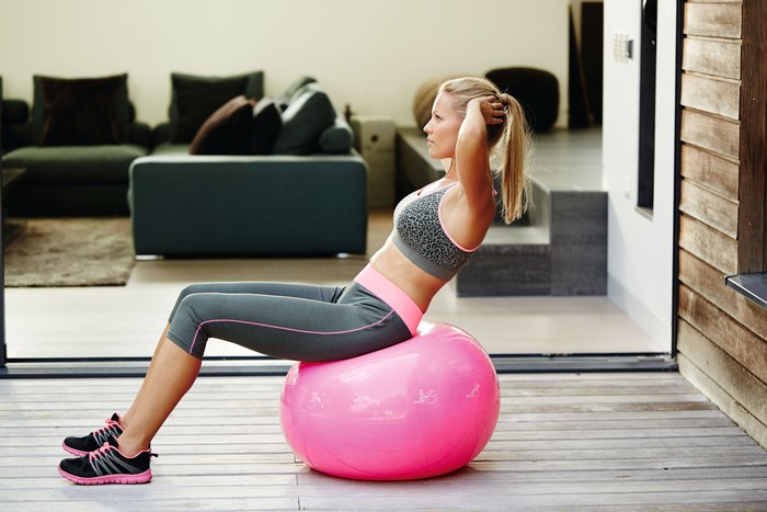 Woman doing sit-ups on a pink exercise ball