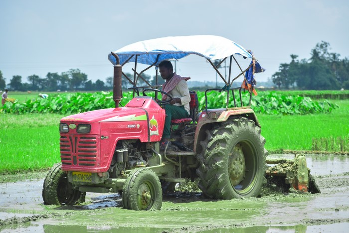 Indian farmer driving a red tractor in a muddy field