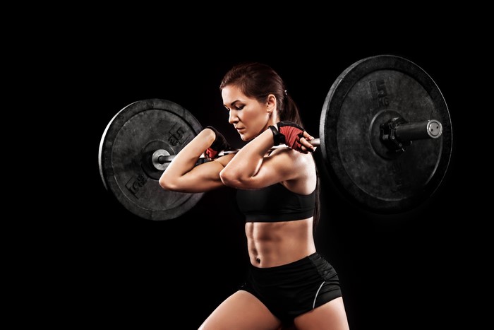Woman lifting barbell on black background