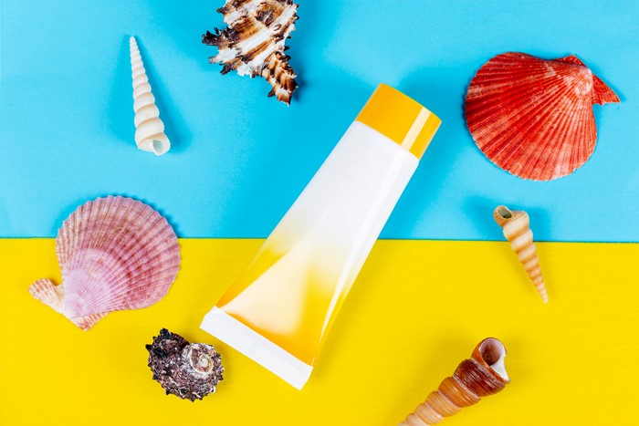 Sunscreen tube and seashells on blue and yellow background