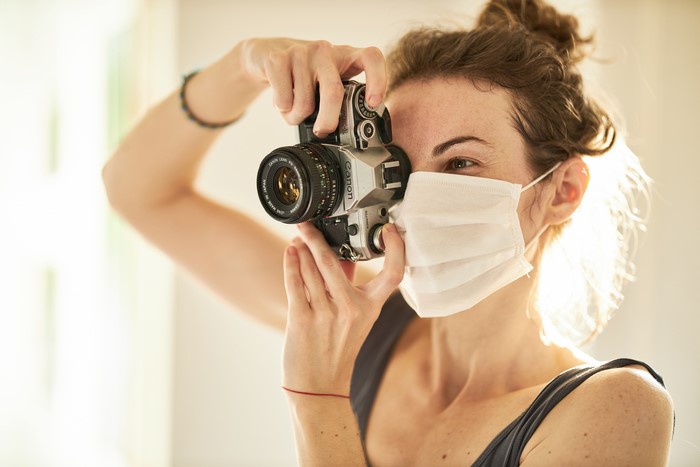 Woman wearing mask taking photo with Canon camera