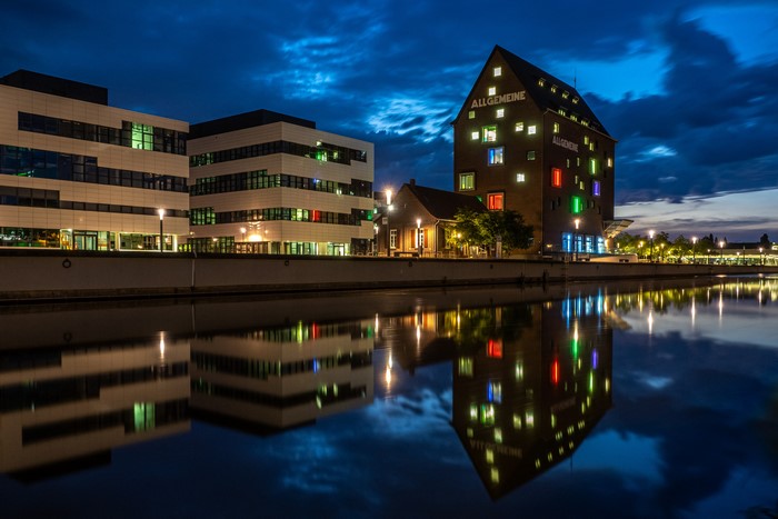 Modern buildings and old tower by river at night
