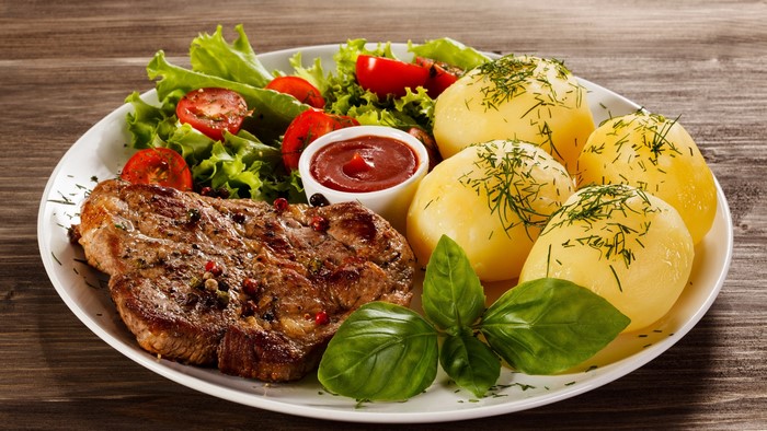 Steak with potatoes, salad, and ketchup on a plate