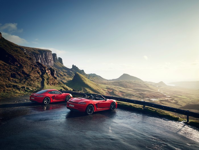 Two red Porsche 718 cars on a scenic mountain road