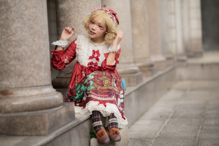 Blonde girl in lolita dress sitting by columns